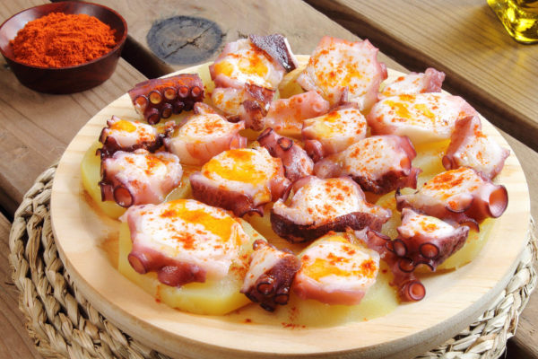 Wooden dish with cooked octopus slices, potatoes and paprika